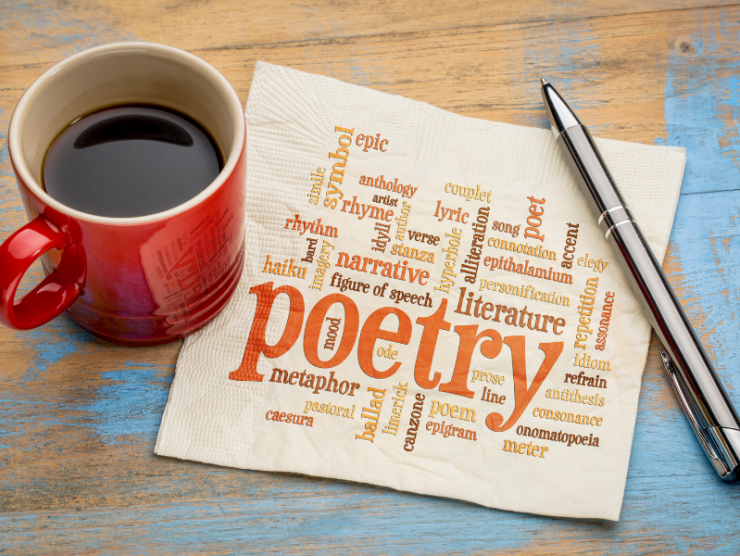 Coffee cup sitting to left of napkin that has poetry and related words embossed on it, with pen on right.