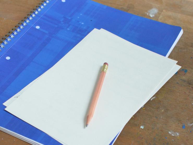 Pencil on top of a sheets of paper and a blue spiral bound notebook